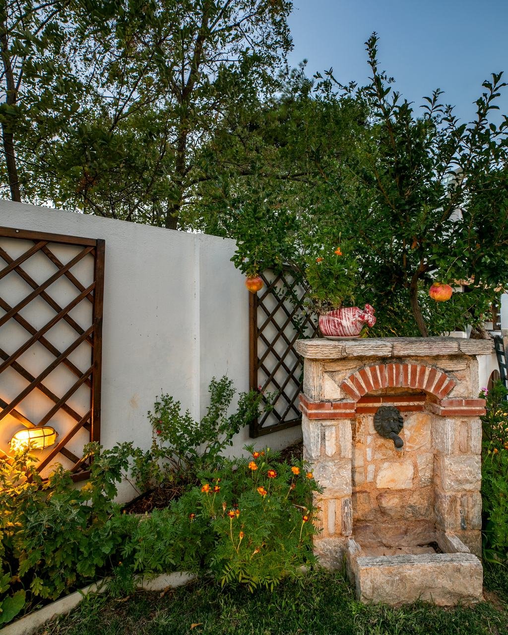 Stone wall fountain among plants, lit in the evening