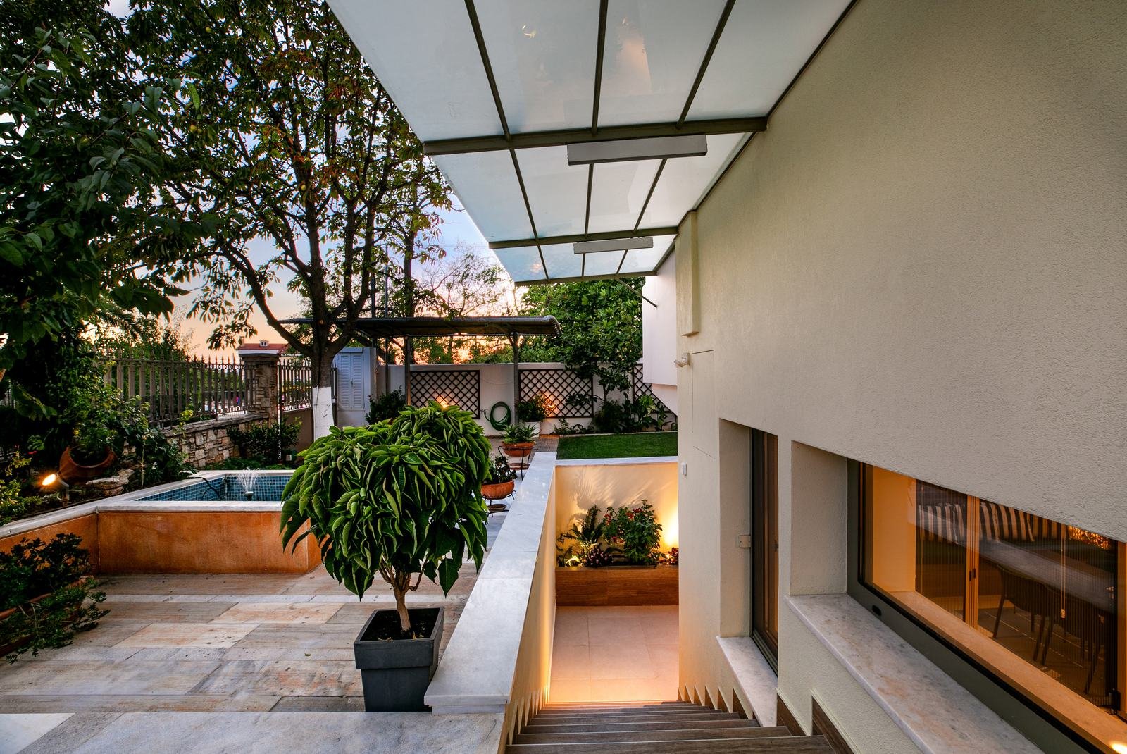 Courtyard at dusk with a tiled fountain pool, a potted tree and lit steps down to the apartment