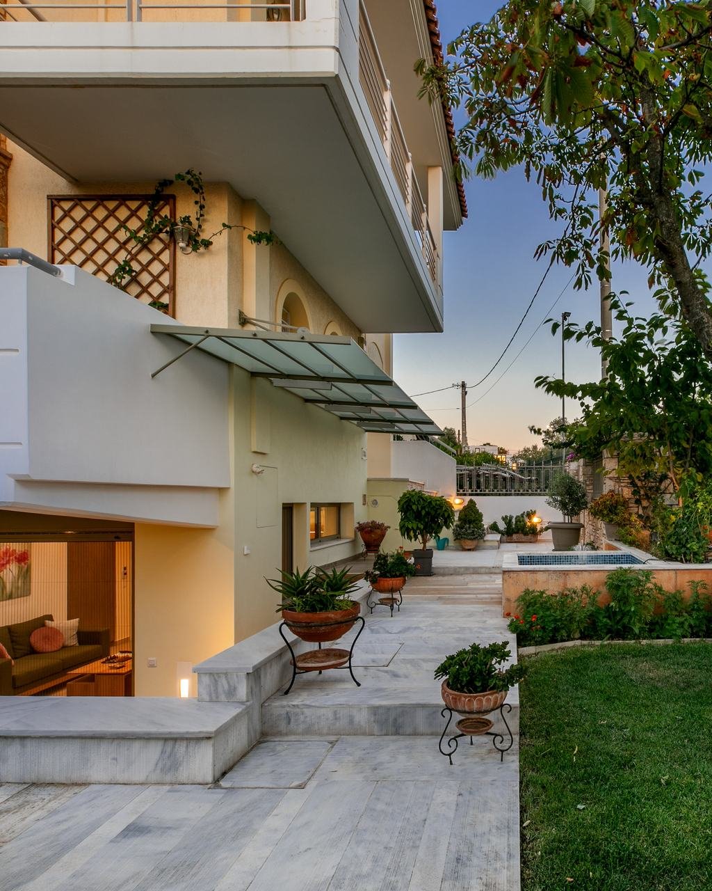 The house at blue hour, the living room glowing behind glass doors that open onto a marble patio